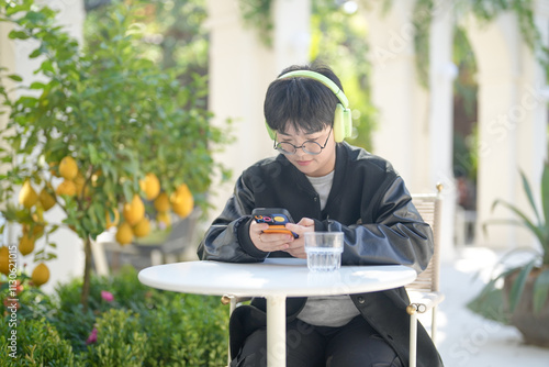 A Chinese woman in her 30s in sporty clothes operates a smartphone while listening to music through headphones at a table in a stylish cafe on Jilu Road in Jing'an District, Shanghai, China. photo