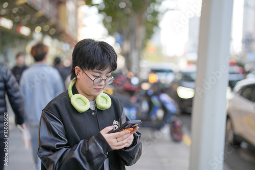 On a cold winter day in December 2024, a Chinese woman in her 30s in sporty clothes operates a smartphone in front of an intersection in Jing'an District, Shanghai, China. photo