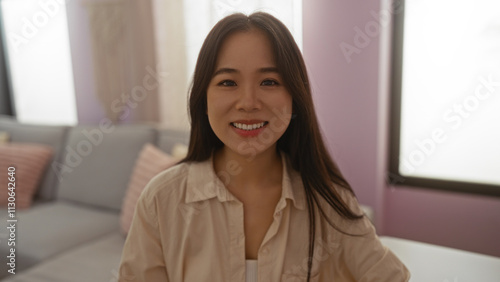 Free Download Young chinese woman smiling warmly in her cozy living room with soft lighting and modern decor, showcasing casual indoor lifestyle - GFXLoad