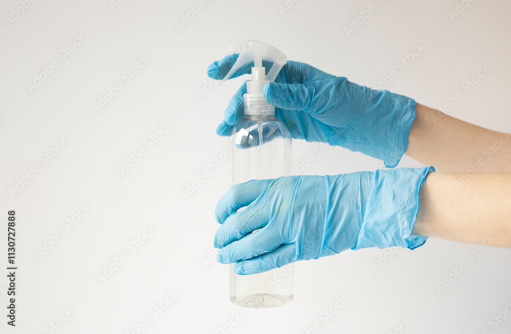 Fototapeta premium Female hands in protective rubber medical gloves of blue color, hold a bottle of antiseptic. on white background isolate.