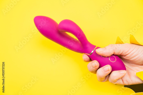 Female hand with magenta vibrator sticking out from yellow paper background. Copy space.