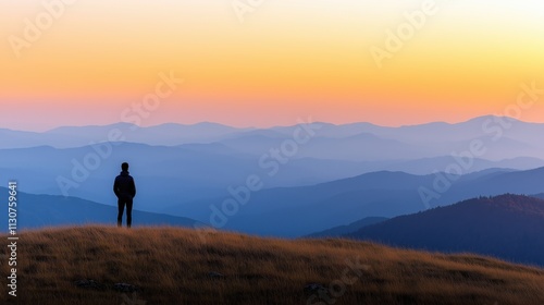 Person standing on hilltop watching gradient sunset over distant mountains