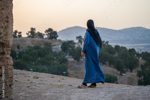 Muslim woman wearing a blue jellaba and a black veil in the site of the Marinid Tombs or Merenid Tombs, monumental tombs on a hill above and north of Fes al-Bali, the old city. Fes, Fès, fez, Morocco photo