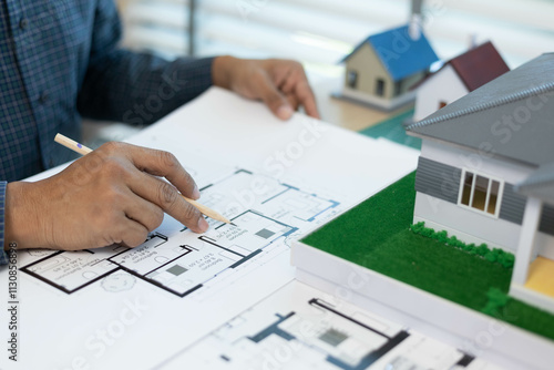 A man is holding a model of a house. The house is a small, two-story home with a slanted roof. The man is wearing a safety vest, which suggests that he is working on a construction site