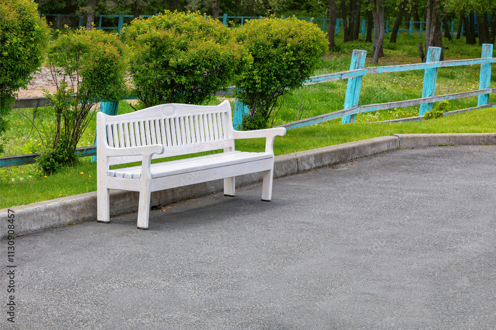 White bench rests peacefully in a serene park surrounded by lush greenery