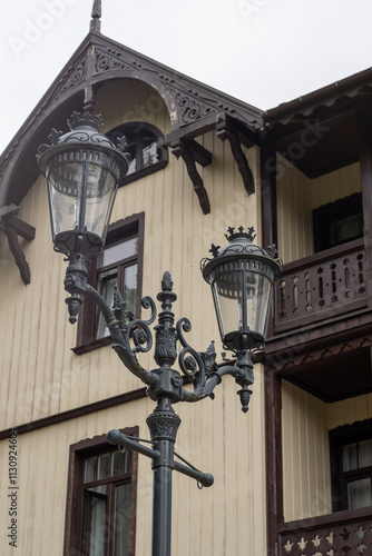 Lantern Old street lamp. A pole with a glass incandescent lampshade. Wooden house