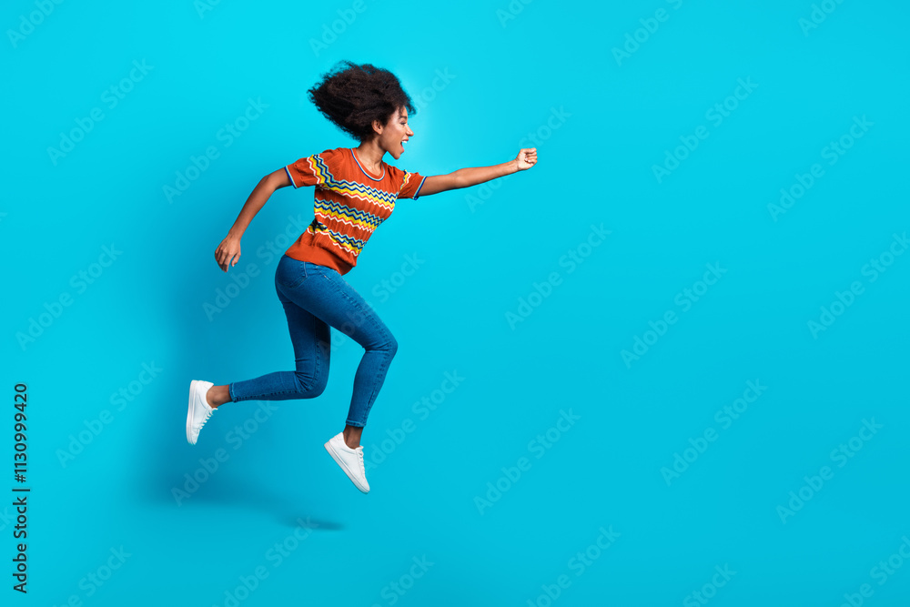 Obraz premium Photo of crazy energetic jumping young funky girl curly hair running for opportunities in life fist up isolated on blue color background