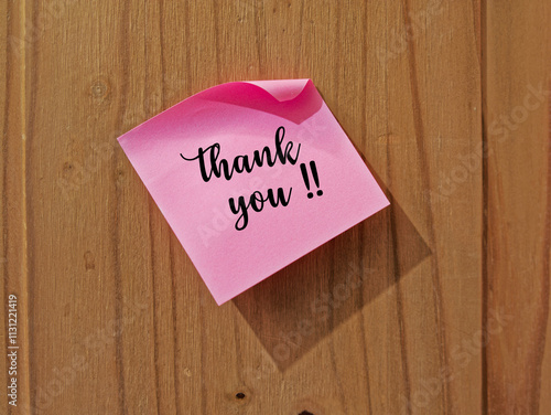 A thank you sticky note on a wooden background