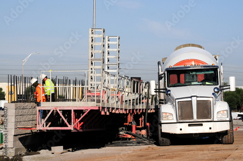 Bricklaying workers construct a barrier at a freeway improvement project, standing on orange scaffolding, with a white cement mixer truck parked nearby supplying the mix for their work photo