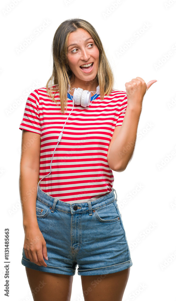 Fototapeta premium Young beautiful woman listening music wearing headphones over isolated background smiling with happy face looking and pointing to the side with thumb up.