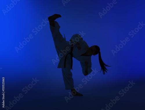 Silhouette of woman in kimono practicing karate on dark blue background photo