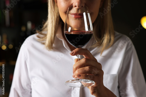 Professional sommelier tasting red wine indoors, closeup photo