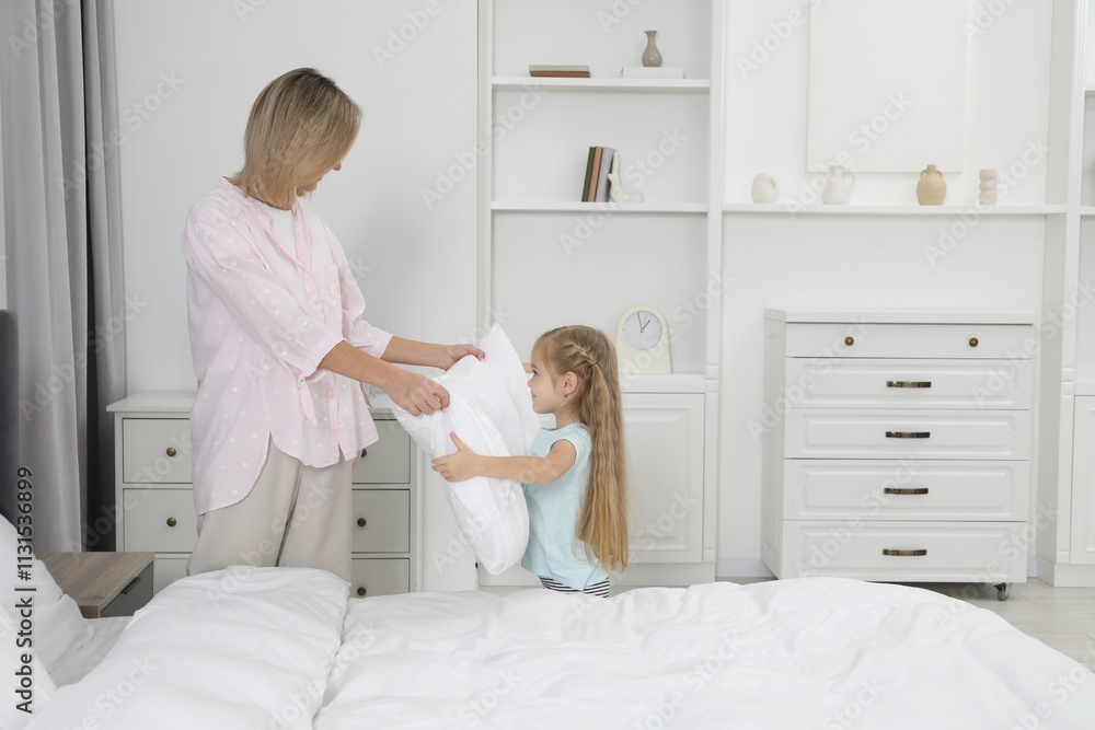 Obraz premium Little girl helping her mother making bed at home