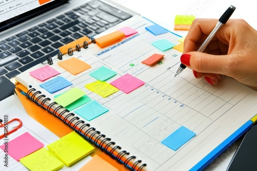 A hand writes in a colorful planner filled with sticky notes and an open laptop, highlighting the importance of clear goals and effective planning for lasting success in life and work