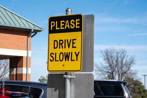 Drive Slowly sign in yellow and black on post in parking lot