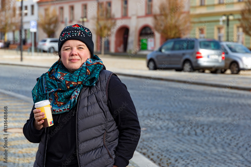 A woman walking through an autumn city and drinking coffee.