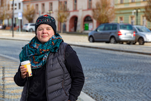 A woman walking through an autumn city and drinking coffee.