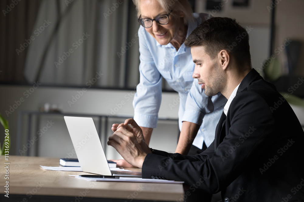 Fototapeta premium Two male female colleague reviewing new corporate software, learn program or business platform, engaged in joint task completion, looking focused, while gaze at laptop screen. Teamwork, modern tech