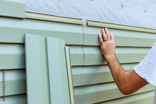 Construction worker carefully aligns, secures new vinyl siding panels on to exterior wall of new house