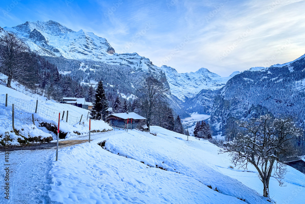 Fototapeta premium Scenic view of Lauterbrunnen Valley, Switzerland with snowcovered mountains Breithorn (middle) and Jungfrau (left) in winter against blue sky with clouds seen from Wengen