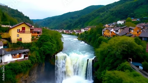 A panoramic view of a village nestled at the base of a majestic waterfall, surrounded by lush greenery photo