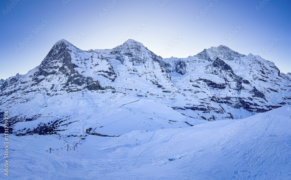 Panoramic view of famous snowcovered Eiger, Moench and Jungfrau mountains (from left to right) in Switzerland in winter early in the morning against blue sky