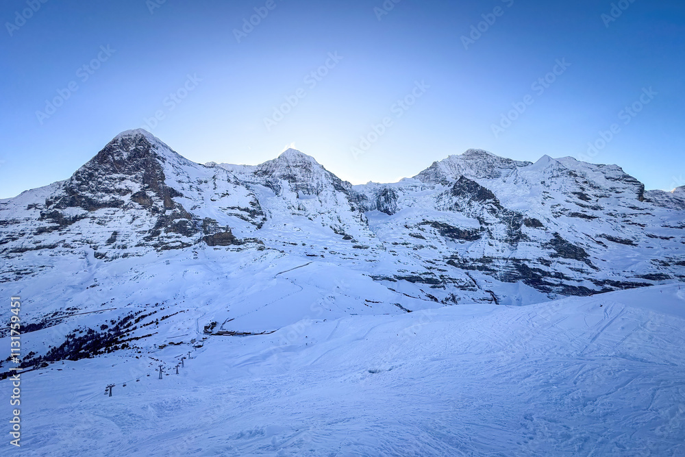Panoramic view of famous snowcovered Eiger, Moench and Jungfrau mountains (from left to right) in Switzerland in winter early in the morning against blue sky