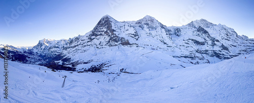 Obraz na płótnie Panoramic view of famous snowcoverd mountains Eiger, Moench and Jungfrau (from left to right) in Switzerland with Grindelwald and Wetterhorn (far left) in winter early in the morning against blue sky w salonie