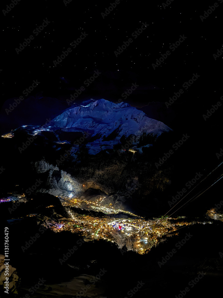 Aerial of illuminated Wengen, Switzerland at night in Winter with blue shining Bietenhorn mountain across
