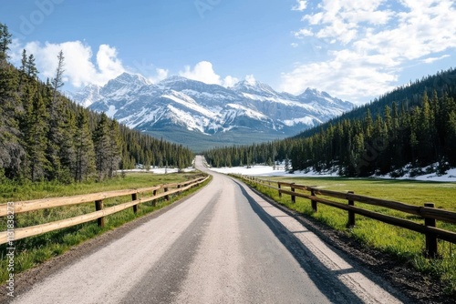 A long road stretches towards a stunning snow-capped mountain range under a blue sky, symbolizing adventure and exploration in a dramatic natural landscape.