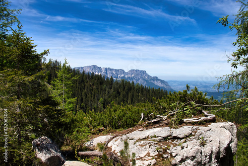 Mountains behind a hill with green trees and a large rock on a spring day in the Bavarian Alps of Germany near the Eagle's Nest.