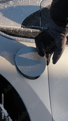 Vertical video of gloved hand inserts power connector into electric vehicle. Charging EV or PHEV in winter. Unrecognizable person connects charging cable to an electric car and charges the batteries photo