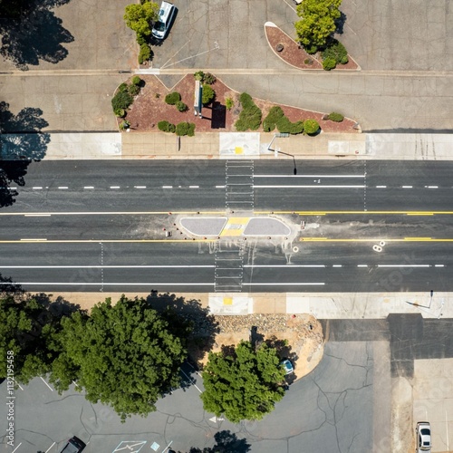 Aerial view of a freshly paved urban roadway with a pedestrian crossing and landscaped medians, surrounded by parking areas and greenery. Ideal for city planning themes.