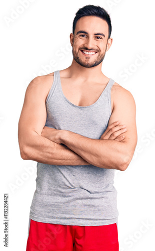 Young handsome man wearing swimwear and sleeveless t-shirt happy face smiling with crossed arms looking at the camera. positive person. photo