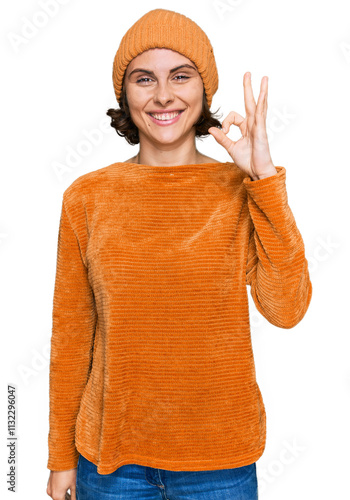 Young hispanic woman wearing casual clothes and wool cap smiling positive doing ok sign with hand and fingers. successful expression.