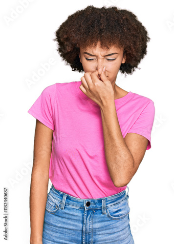 Young hispanic girl wearing casual clothes smelling something stinky and disgusting, intolerable smell, holding breath with fingers on nose. bad smell photo