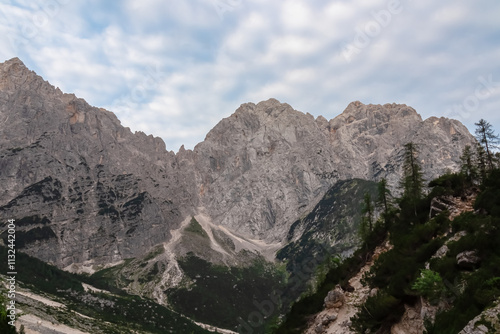 Hiking trail with scenic view of rugged majestic mountain peaks of Julian Alps seen from Krnica valley, Vrsic pass, Slovenia. Wanderlust wild Slovenian Alps. Ridges with sharp edges and steep cliffs photo