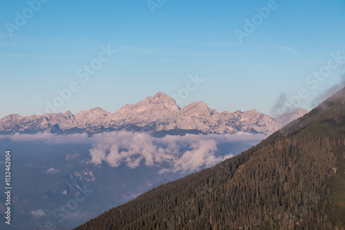 Rugged mountain peak Triglav seen from Begunjscica, Loibl Pass, Karawanks, Slovenia Austria. Wanderlust in Austrian Slovenian Alps in summer. Slopes covered with lush green dense forest. Hiking trail photo