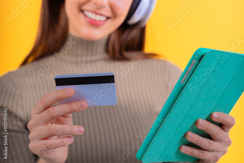 Unrecopgnizable woman holding a tablet and credit card against a bright yellow background.