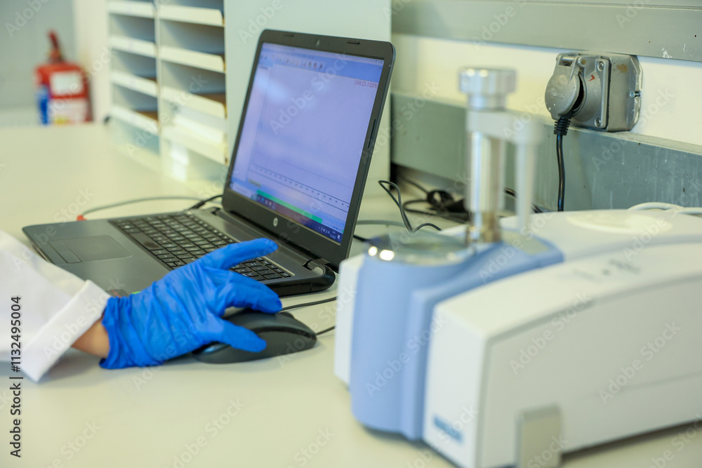Scientist analyzing data using a laboratory computer and advanced FTIR spectrometer. Professional research environment for chemical analysis, technology, and laboratory science in modern industries