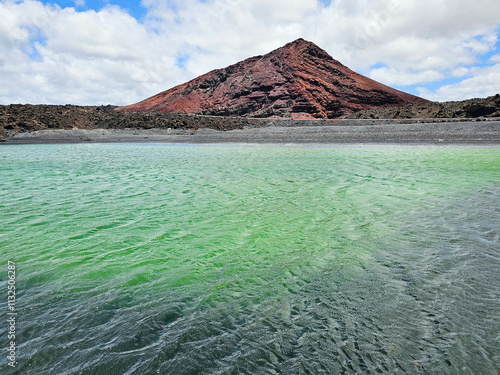 Les eaux vert émeraude du lac vert de Montana Bermeja se déploient au pied de la montagne rougeâtre, offrant un contraste saisissant sous un ciel lumineux. photo