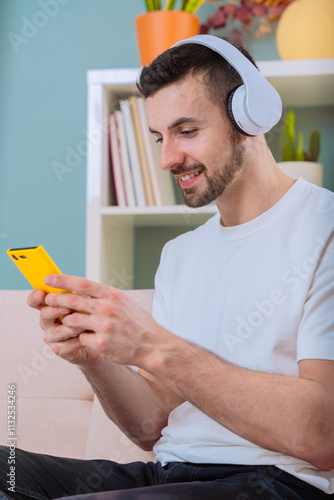 Man using smartphone and headphones while sitting in a cozy living room.Vertical