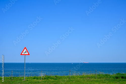 Warning sign before crashing on the edge of a cliff by the sea on a meadow photo