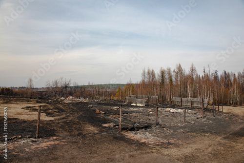Black ashes on the site of a burnt house with a burnt fence. A completely burnt house after a fire.