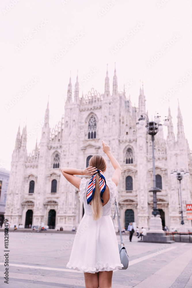 Obraz premium back view of a girl in a white dress with handbag and handkerchief in her head. girl shows on Duomo Cathedral, Milan, Italy.