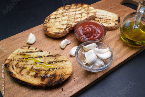 fette di pane tostato con ciotole di aglio,  ketchup e ampollina di olio sul tagliere