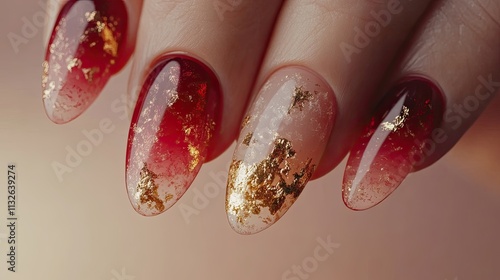 Close-up of elegantly manicured nails showcasing a stunning ombre design in shades of red and gold foil accents. The sheer polish allows for a delicate, luxurious look.