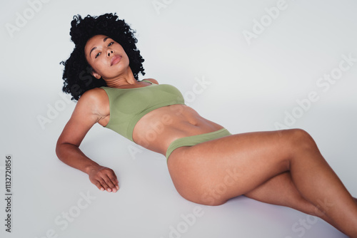 Confident young woman with natural beauty posing in green activewear against a bright studio backdrop