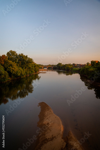 A scenic view of a calm river at sunset with a sandbar and lush greenery was captured in Fredericksburg, Virginia.