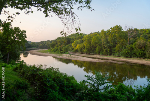 Scenic view of the Rappahannock River surrounded by lush green trees and foliage in Fredericksburg, Virginia, during sunset.
